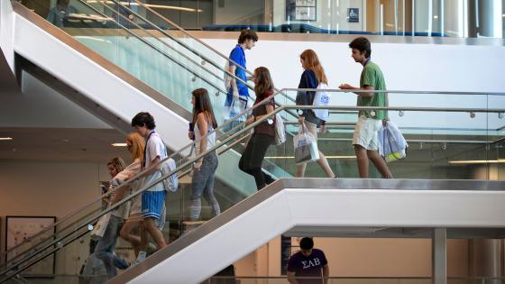 A group of students descend the steps in the student center wearing SBU backpacks.