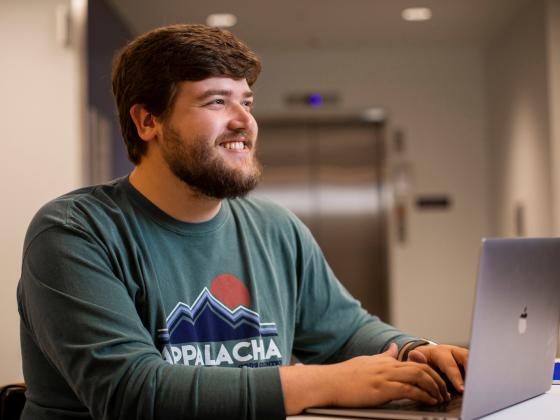 A male student sits at a laptop in class.